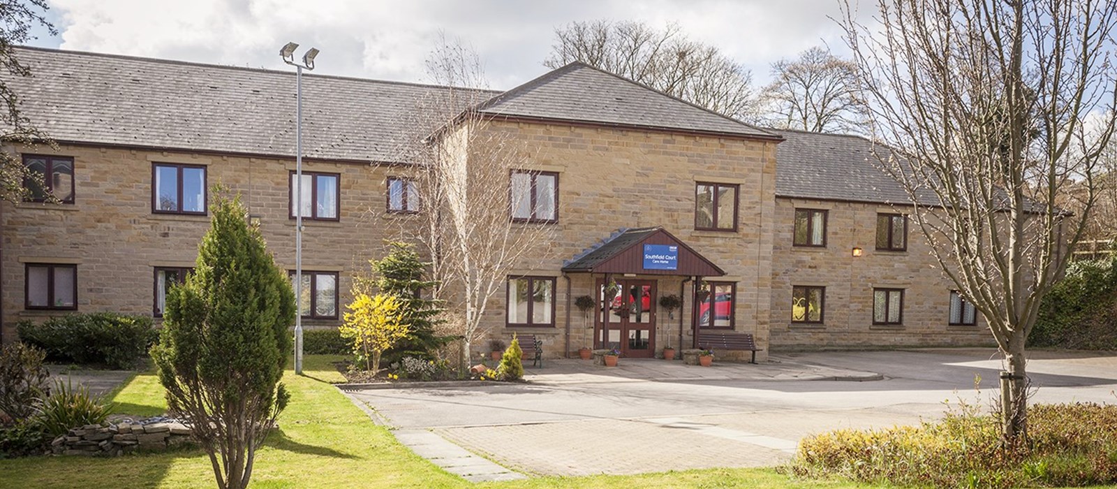 Front view of Southfield Court Care Home in Almondbury, showing the brick building, welcoming entrance, and surrounding green lawn with trees.