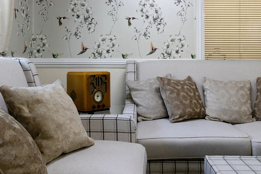 Photo of the sitting room in Astley Grange Care Centre, with two grey sofas and an old radio visible