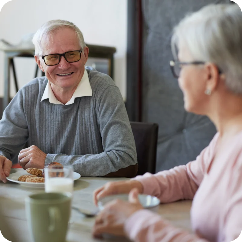 Photo of an elderly couple seated around a breakfast table smiling at one another, with rounded edges