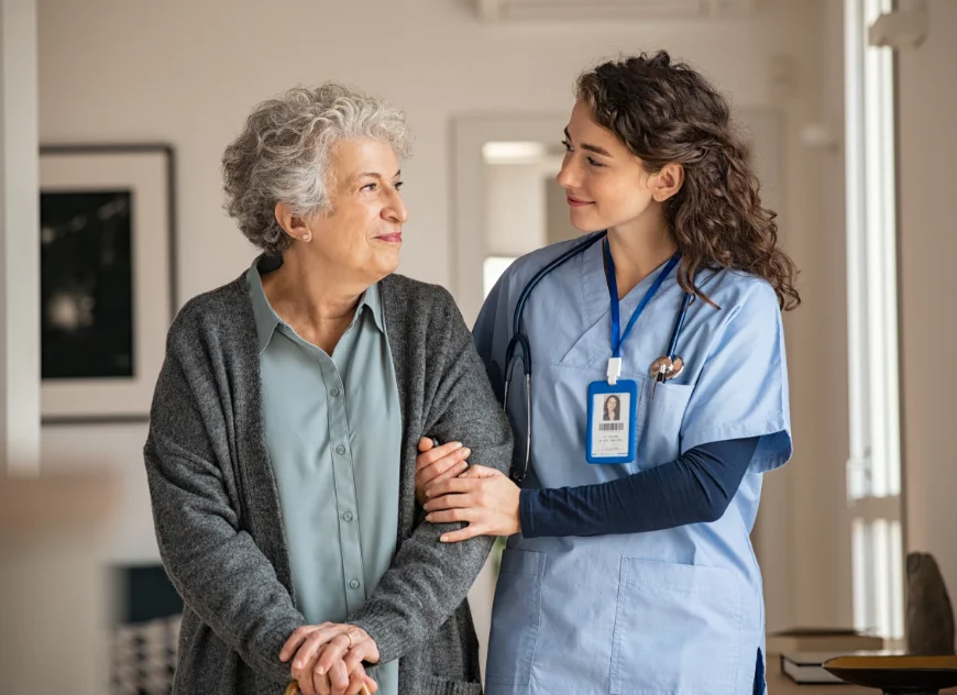 Photo of a nurse holding the arm of an elderly woman in the corridor of a care home