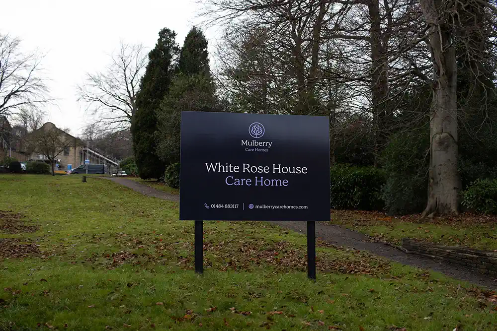 Photo of a sign outside White Rose House Care Home taken from the bottom of a path leading from Huddersfield Road to the main entrance