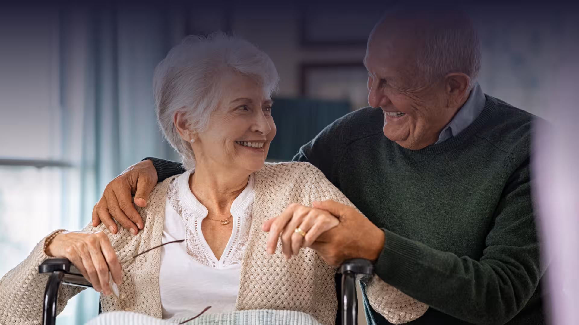 Senior husband embracing disabled wife sitting on wheelchair at nursing home